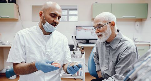 An older man listening to a dentist explain the preliminary treatments he might need to receive dental implants