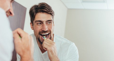 Man smiling while brushing his teeth