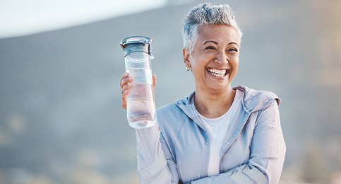 Woman smiling with water bottle on hike outside