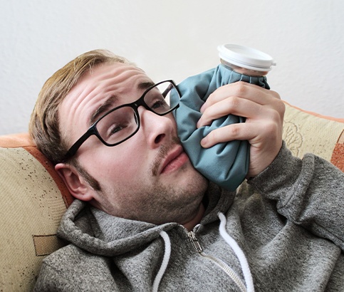 Man in need  of emergency dentistry holding ice pack to jaw