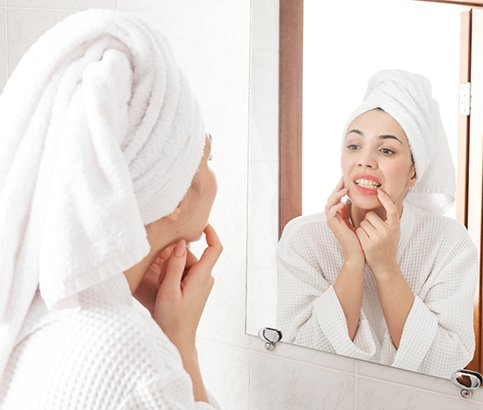 Woman in white robe looking at gums in reflection