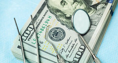 A stack of money with dental instruments lying on top of it