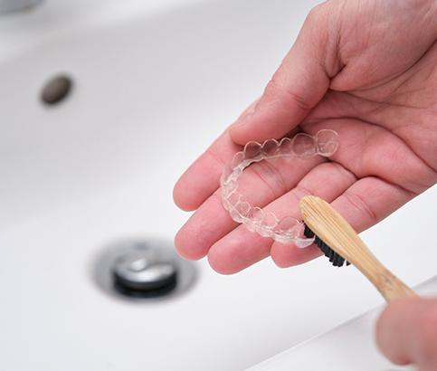 Patient using toothbrush to clean aligners in sink