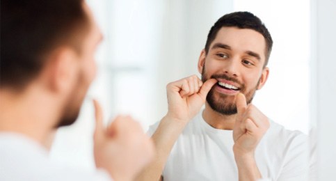 man flossing in bathroom mirror  