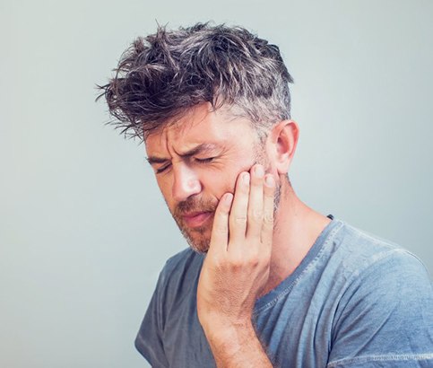 a man touching his cheek due to failed dental implant