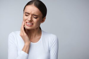 Woman in a white shirt holding her hand to her jaw in pain